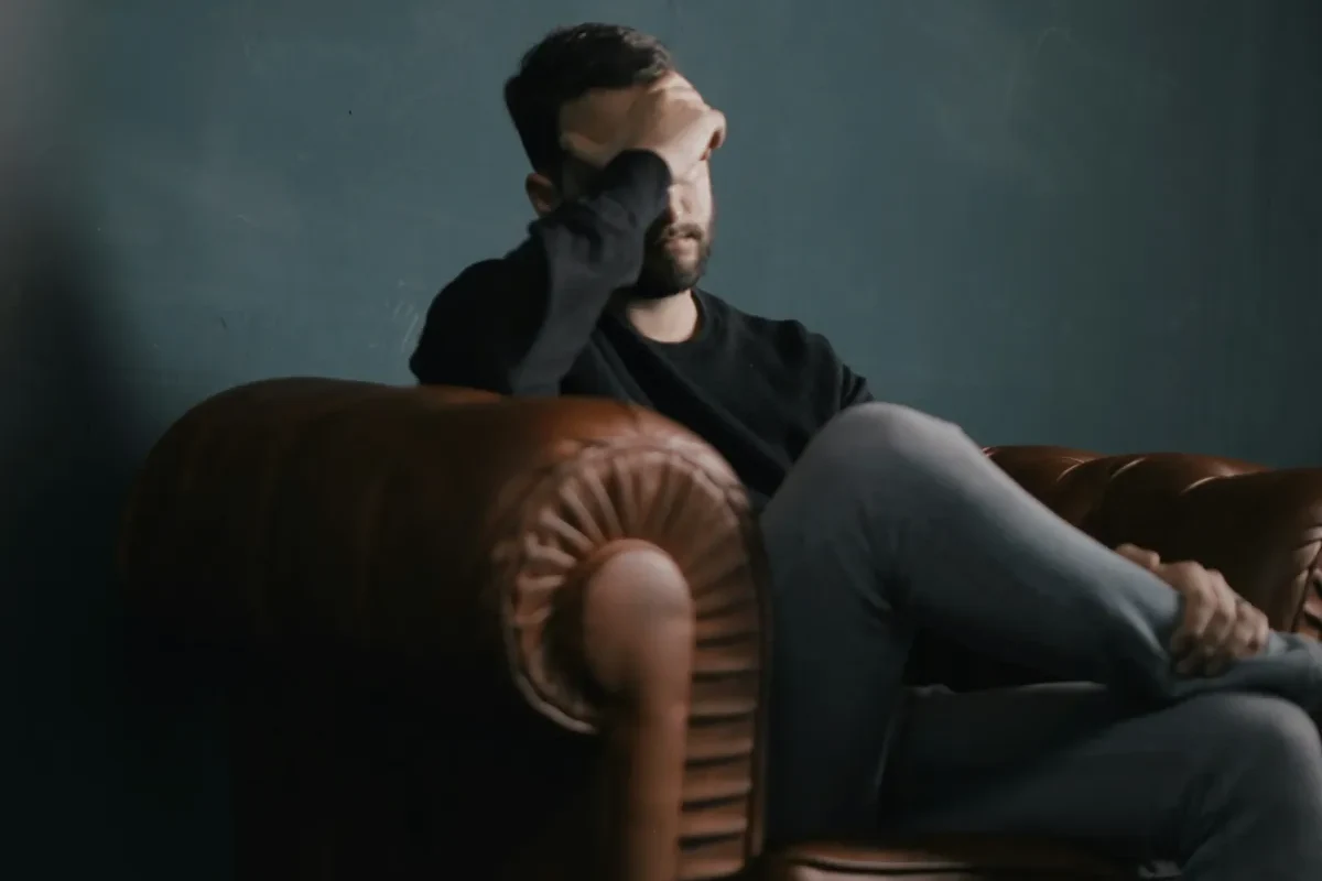 Man sitting alone on a leather couch with his hand over his eyes, reflecting the weight of low mood and depression