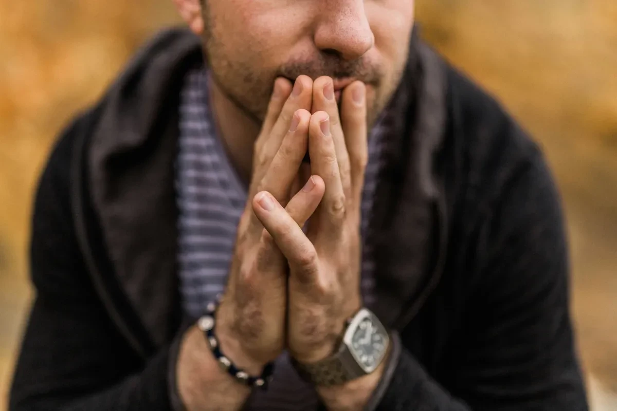 Man with hands clasped in front of his mouth, deep in thought, reflecting the weight of grief and loss